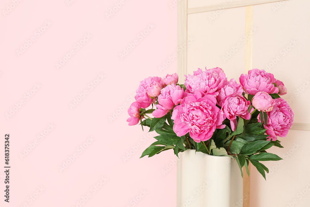 Vase of pink peonies with dressing screen near color wall