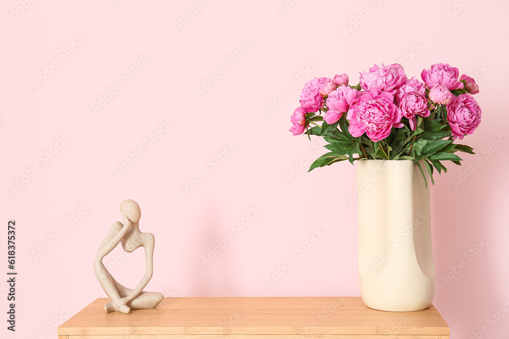 Vase of pink peonies and figurine on shelving unit near color wall