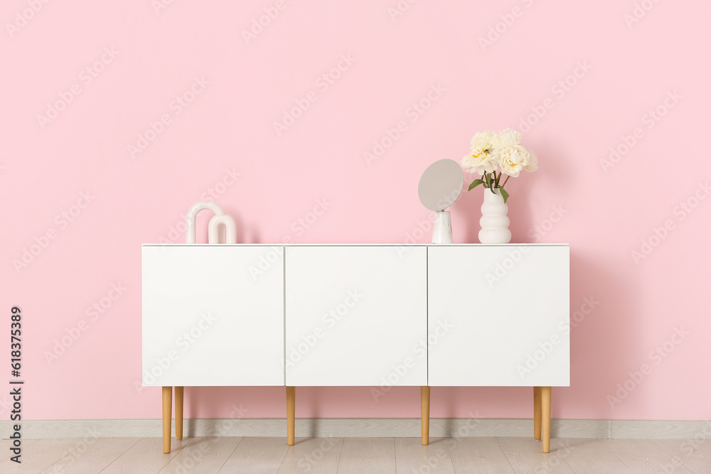 Vase of white peonies and mirror on dresser near pink wall