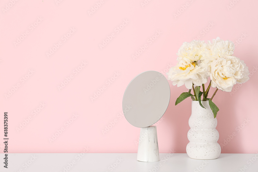 Vase of white peonies and mirror on dresser near pink wall