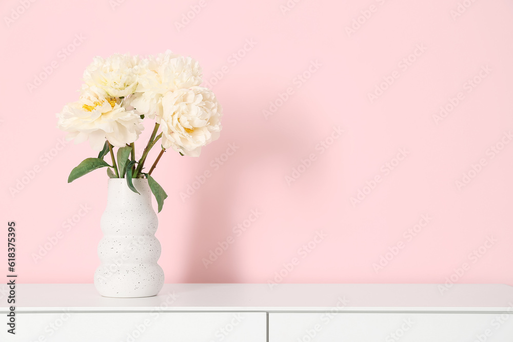 Vase of white peonies on dresser near pink wall