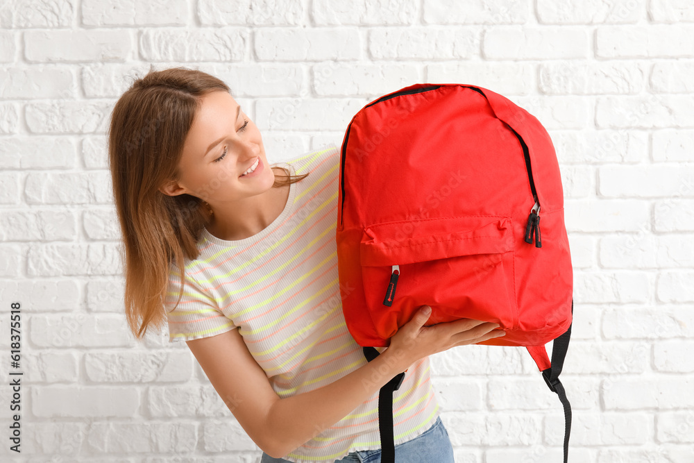 Female student with backpack on white brick background