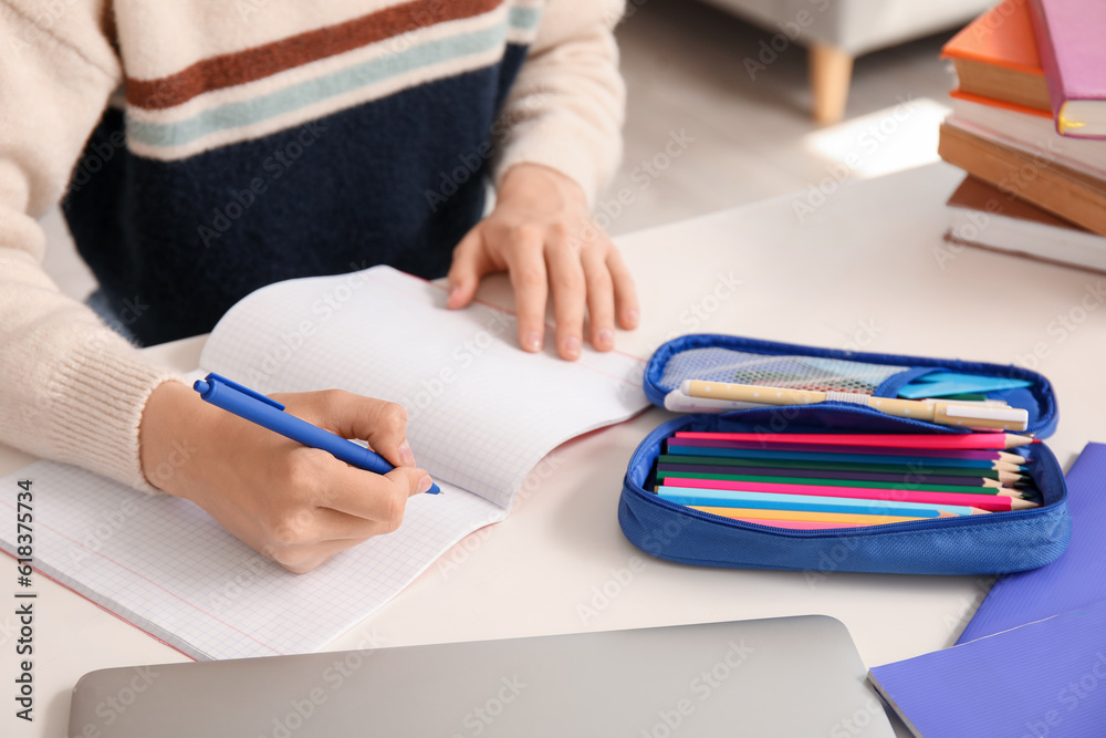 Female student with pencil case writing in copybook at table, closeup