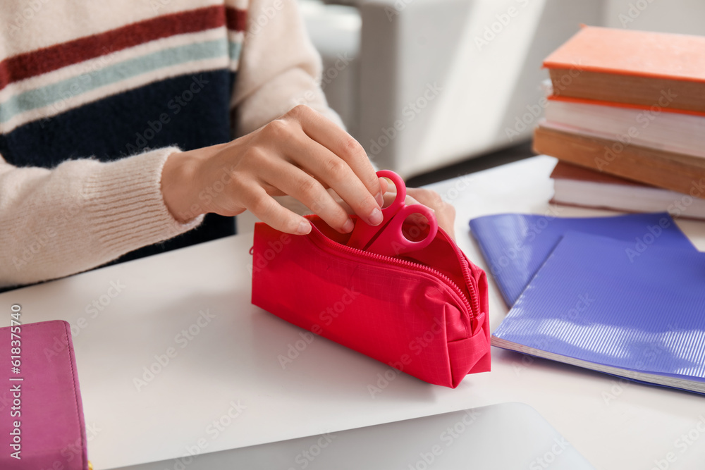 Female student taking scissors from pencil case at table, closeup