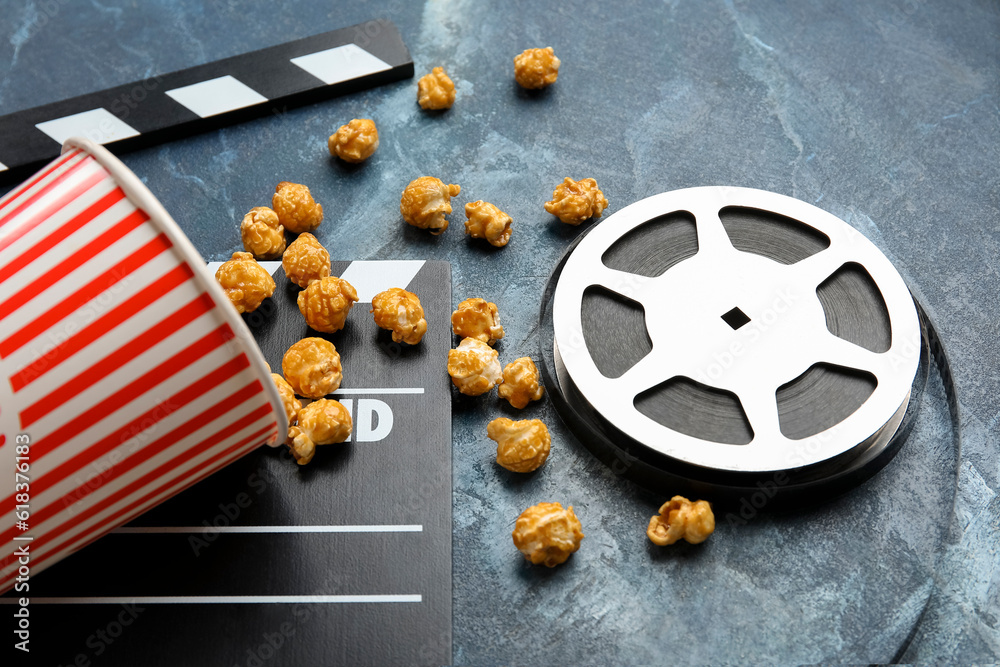 Bucket with tasty popcorn, clapperboard and film reel on blue background