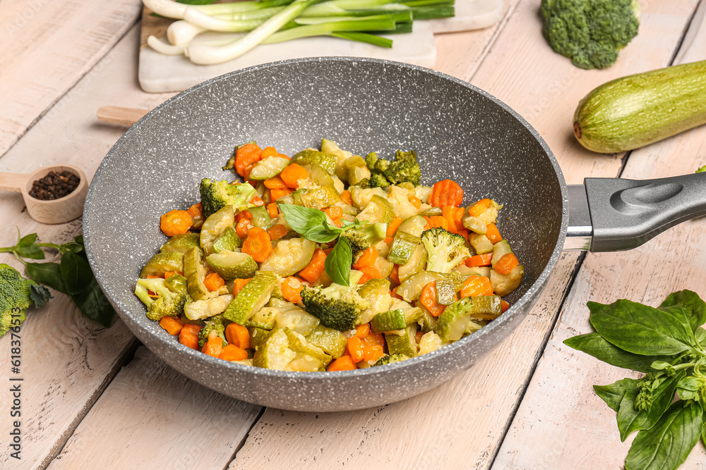 Frying pan with different vegetables on light wooden background