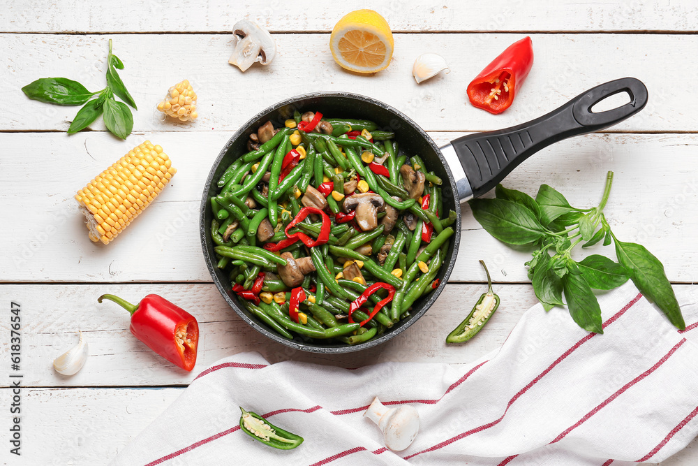 Frying pan with different vegetables on light wooden background