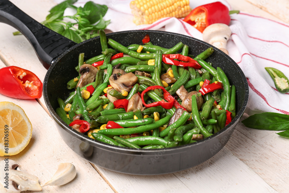 Frying pan with different vegetables on light wooden background