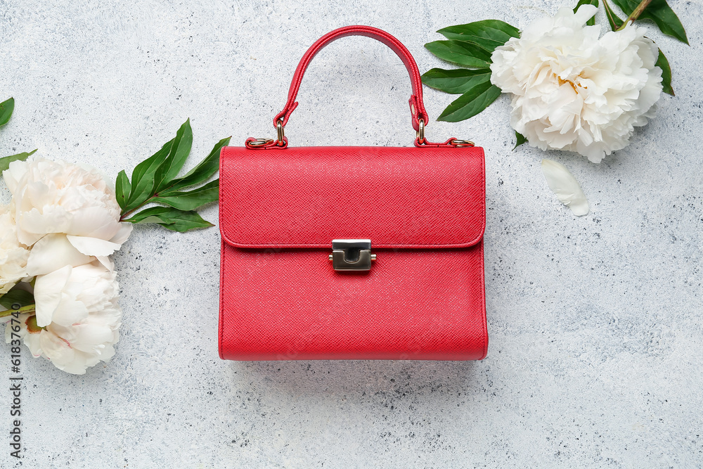 Stylish female bag and beautiful peony flowers on light background