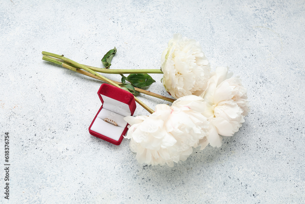 Box with beautiful female ring and peony flowers on light background