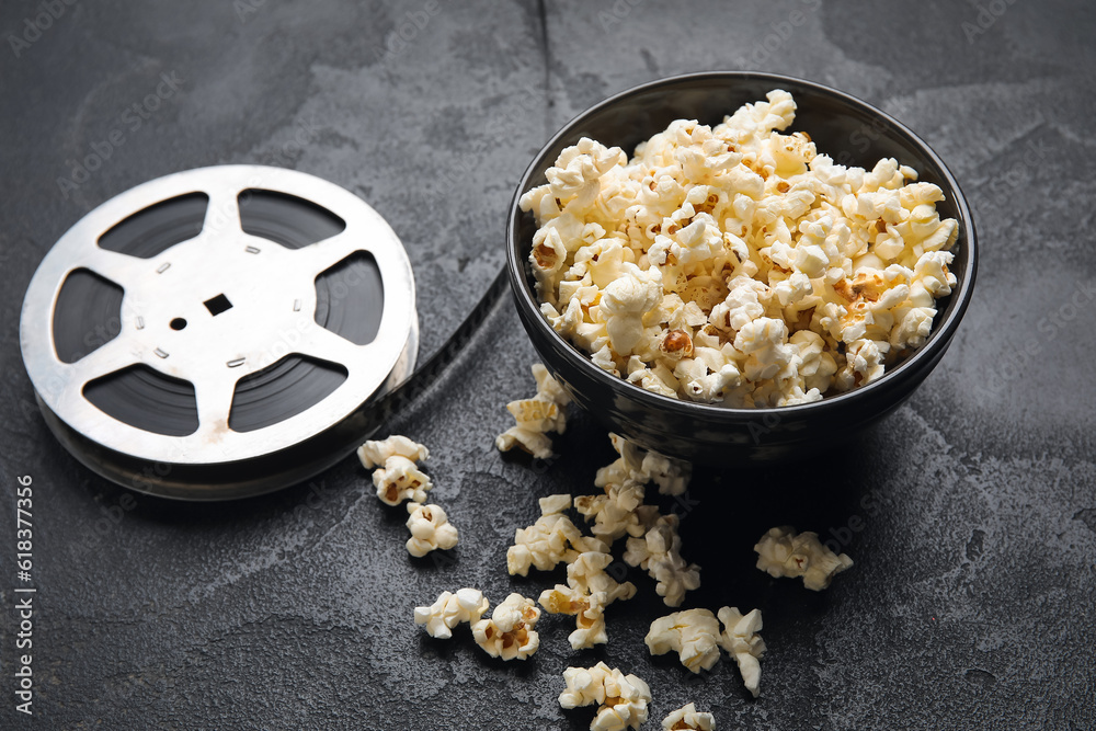 Bowl with tasty popcorn and film reel on black background