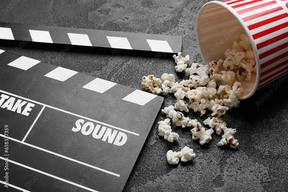 Bucket with tasty popcorn and clapperboard on black background