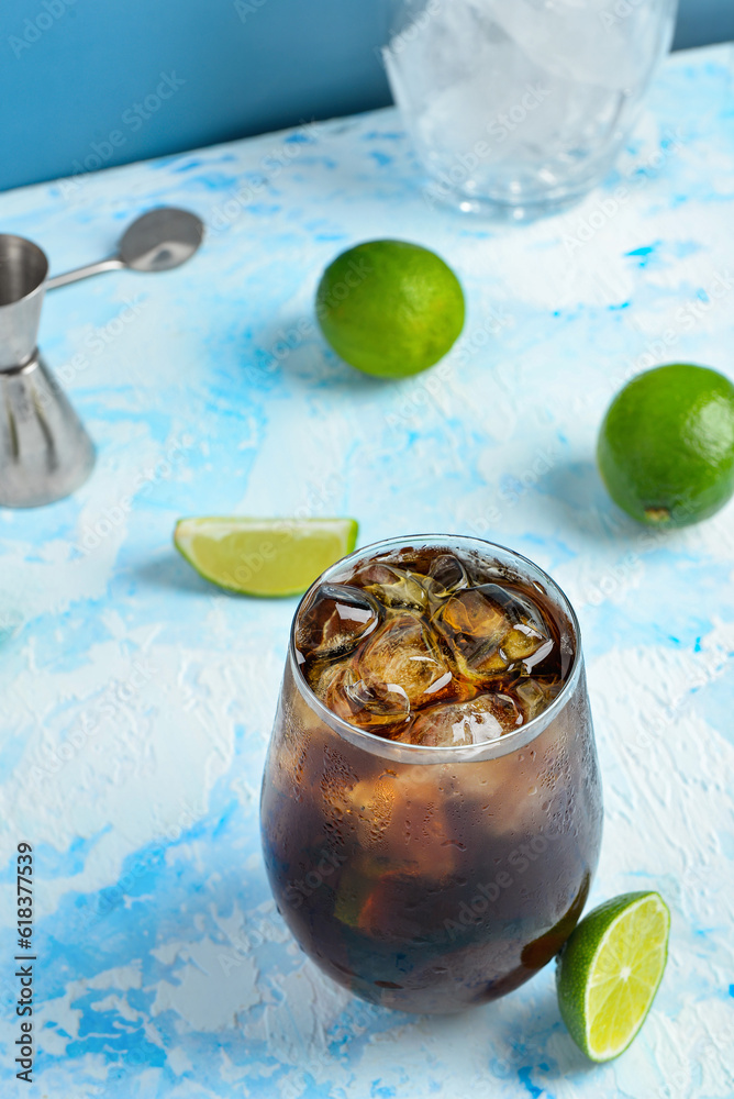 Glass of cold Cuba Libre cocktail on blue background