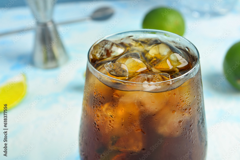 Glass of cold Cuba Libre cocktail on blue background