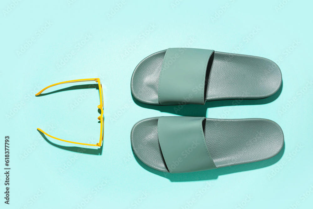 Turquoise flip-flops with sunglasses on color background