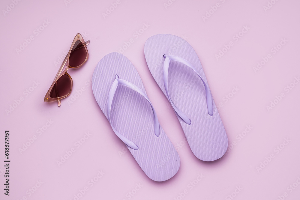 Lilac flip-flops with sunglasses on color background