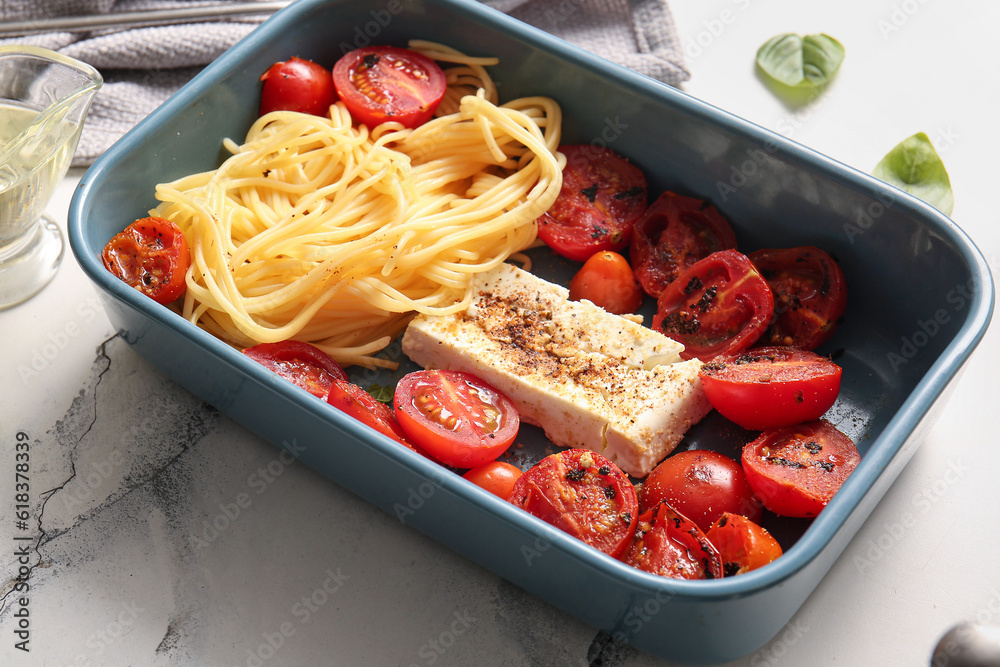 Baking dish of tasty pasta with tomatoes and feta cheese on white marble background