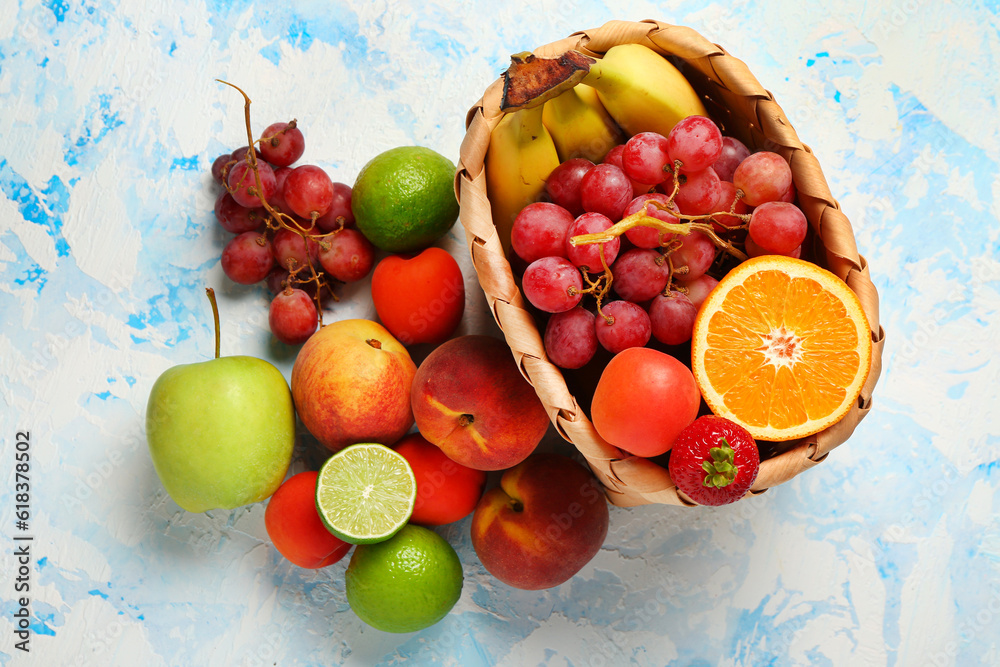 Wicker basket with different fresh fruits on light blue background