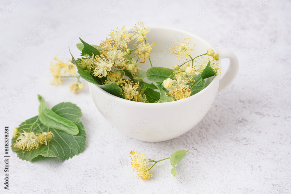 Cup of fresh linden flowers on light background