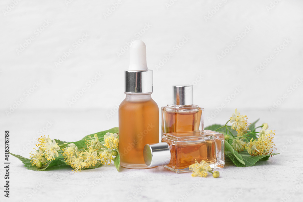 Bottles of essential oil and fresh linden flowers on light background