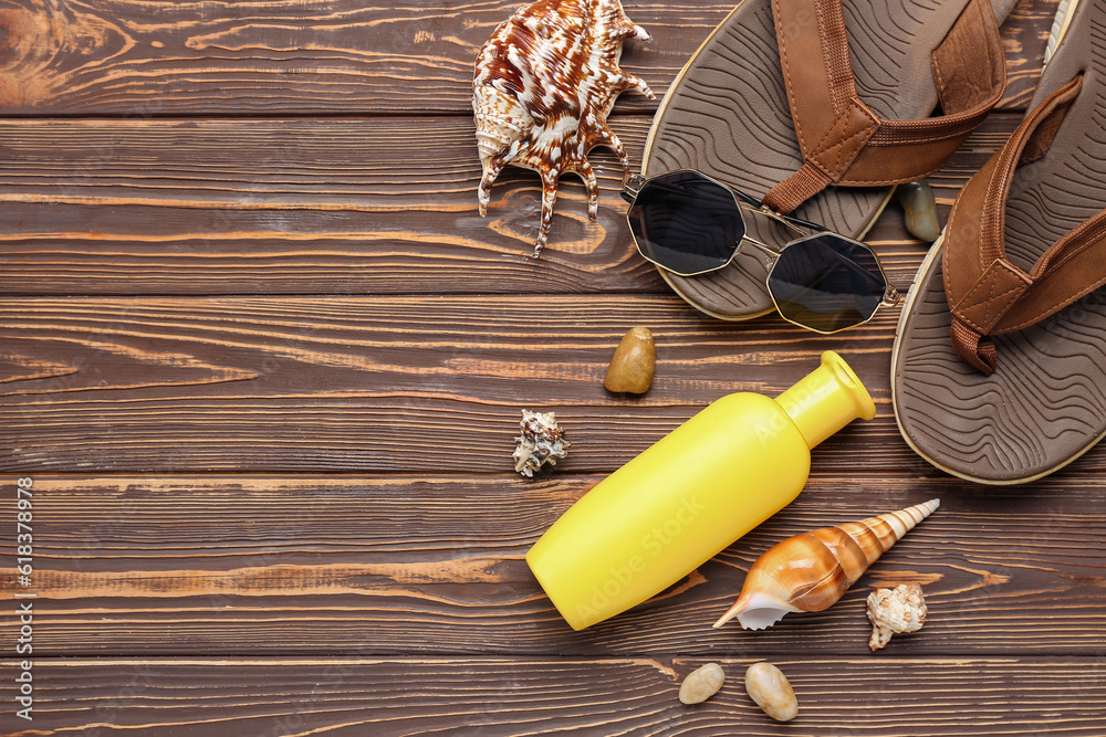 Flip flops with sunglasses, seashells and bottle of sunscreen cream on wooden background