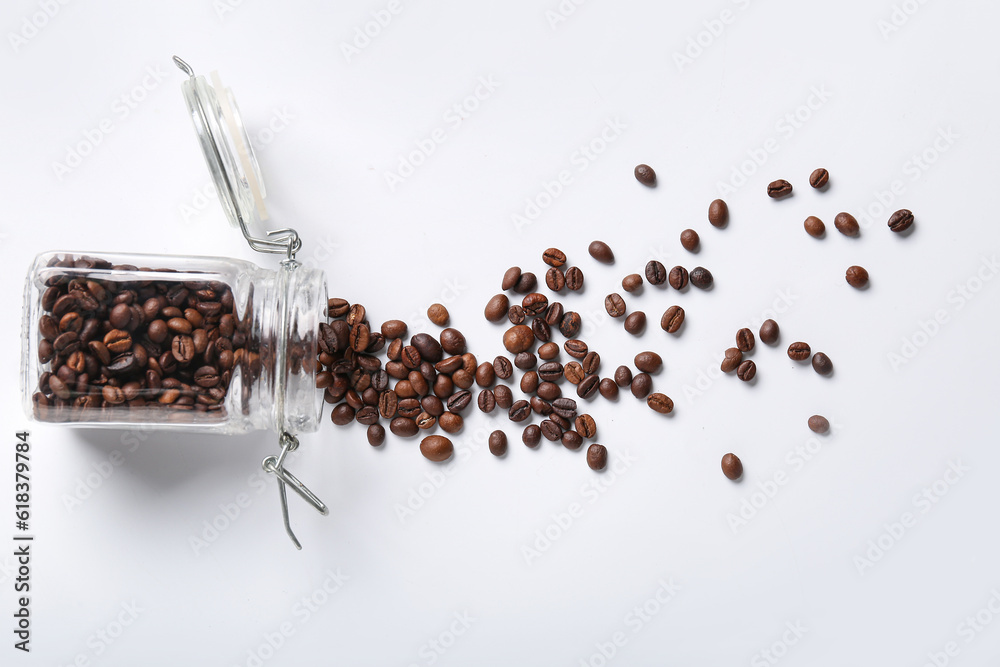 Glass jar with scattered coffee beans on white background