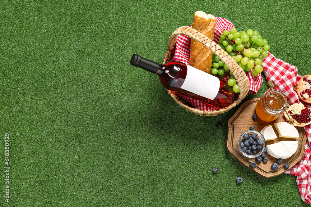 Composition with tasty food for picnic, honey and wine on green background