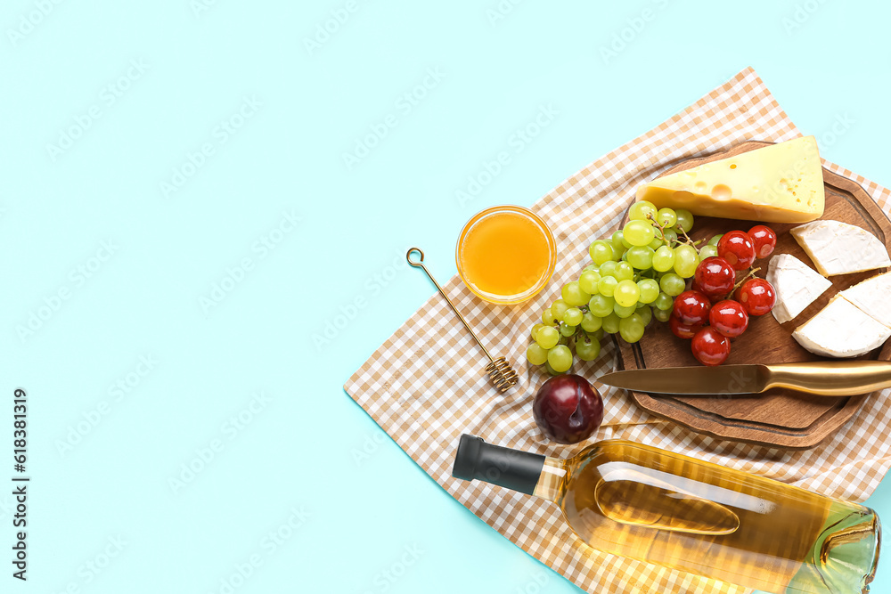 Composition with tasty food for picnic, bottle of wine and honey on blue background