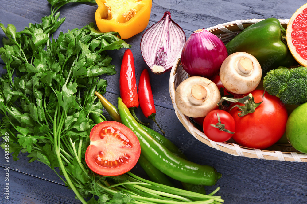 Basket with fresh ripe vegetables on blue wooden background, closeup