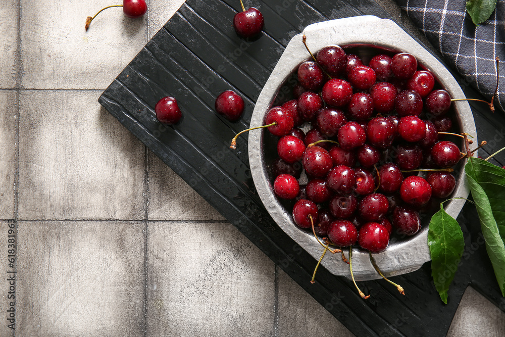 Board with metal plate of sweet cherries on grey tile background