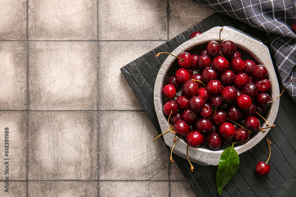 Board with metal plate of sweet cherries on grey tile background