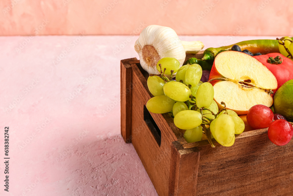 Wooden box with different fresh fruits and vegetables on pink background, closeup