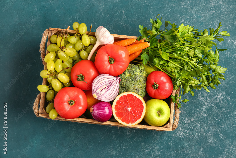 Wooden box with different fresh fruits and vegetables on green background