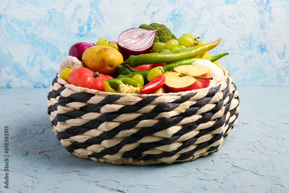 Wicker bowl with different fresh fruits and vegetables on blue background