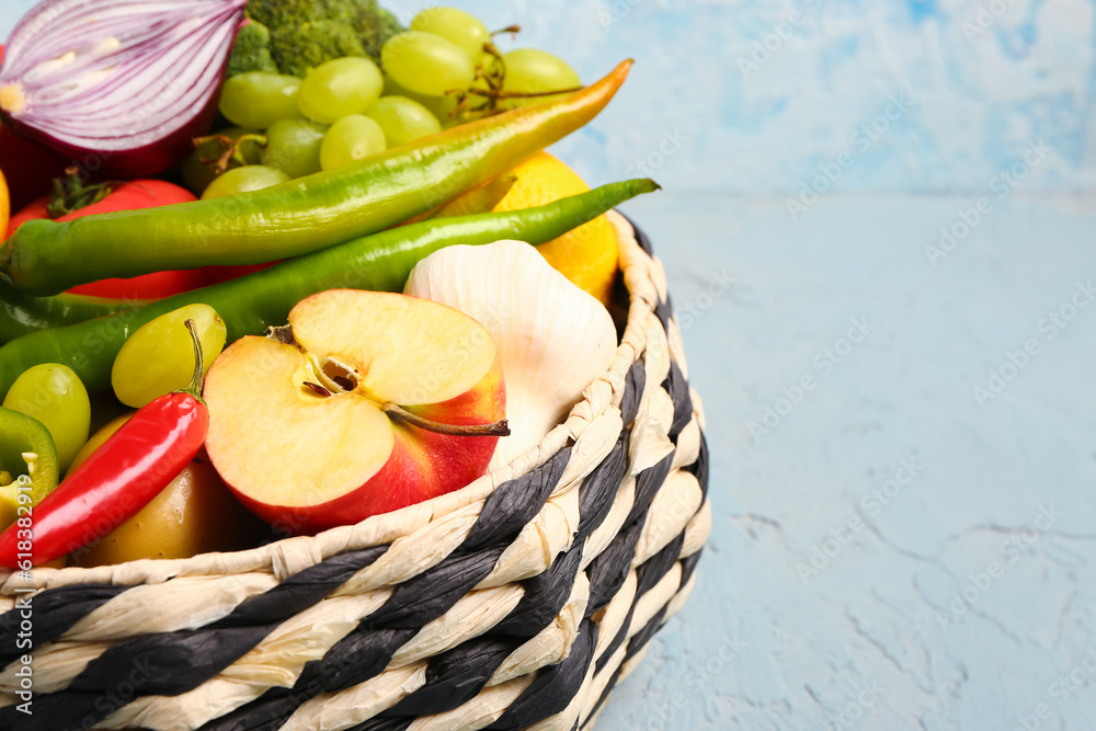 Wicker bowl with different fresh fruits and vegetables on blue background, closeup