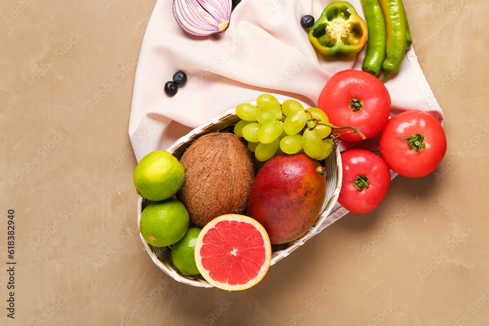 Wicker bowl with different fresh fruits and vegetables on brown background