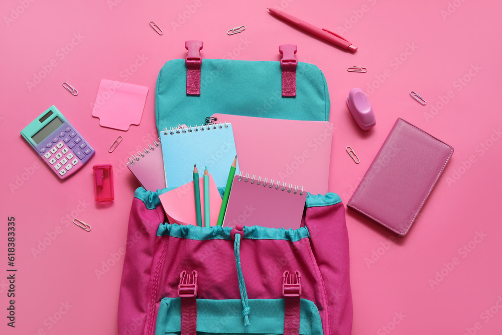 Colorful school backpack with notebooks, calculator and pencils on pink background