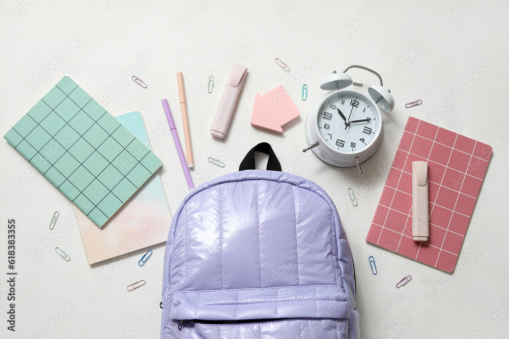 Lilac school backpack with notebooks, alarm clock and markers on white background