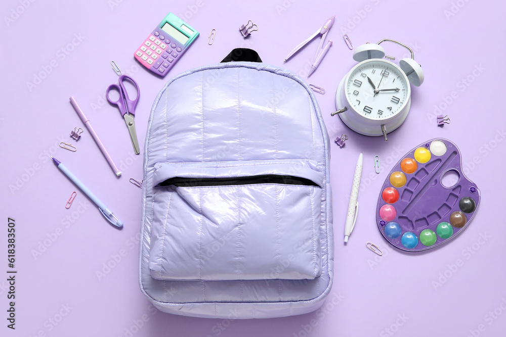 School backpack with alarm clock, calculator and watercolors on lilac background