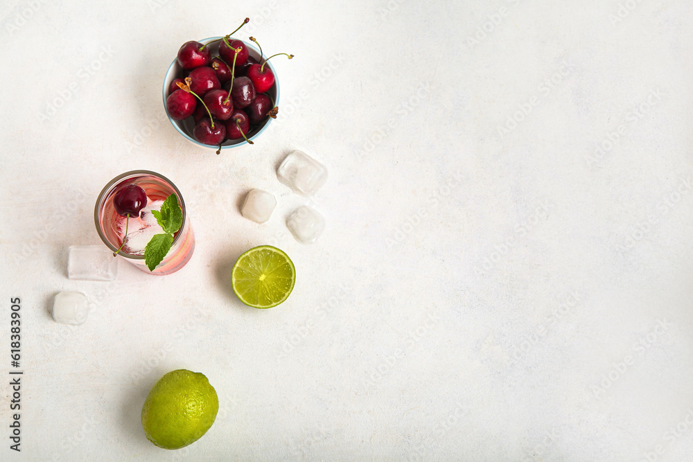 Glass of tasty cherry lemonade, limes and bowl with berries on white background