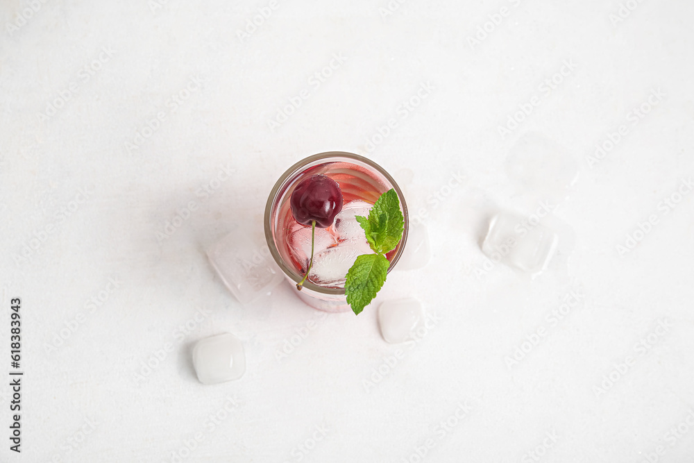 Glass of tasty cherry lemonade with ice cubes and mint on white background