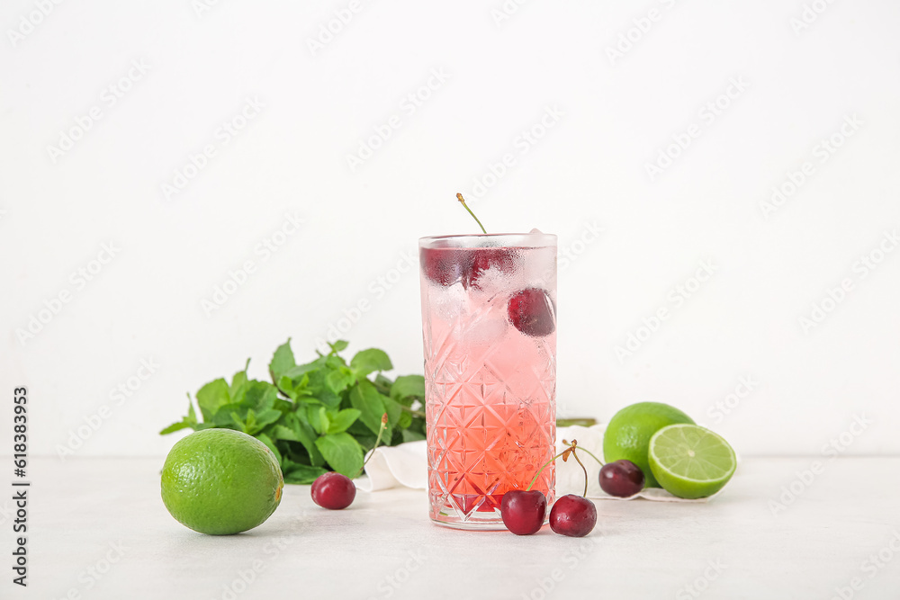 Glass of tasty cherry lemonade with limes and mint on white background