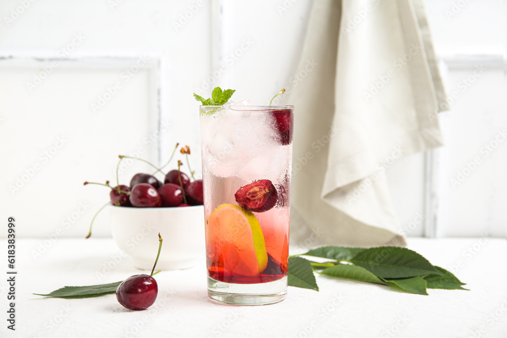 Glass of tasty cherry lemonade and bowl with berries on white background