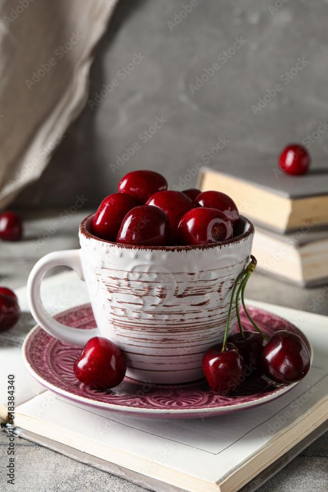 Cup with sweet cherries and books on grey background, closeup