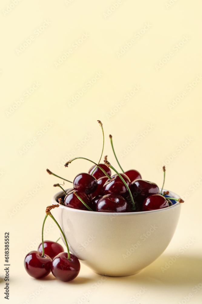 Bowl with sweet cherries on yellow background