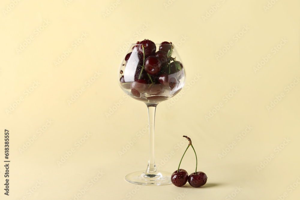 Glass with sweet cherries on yellow background