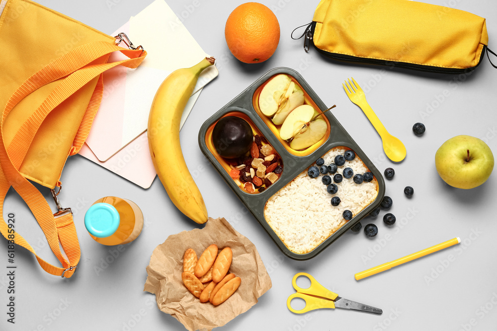 Backpack, stationery and lunchbox with tasty food on grey background