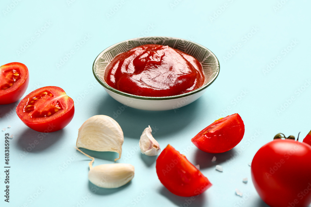 Bowl with tomato paste and fresh vegetables on blue background