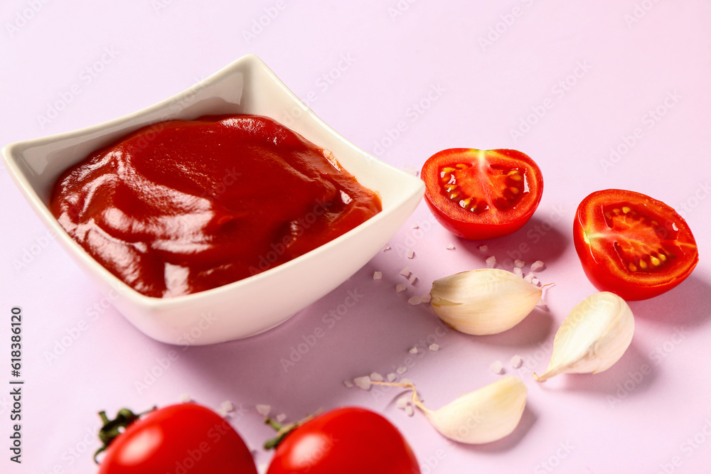 Bowl with tomato paste and fresh vegetables on lilac background