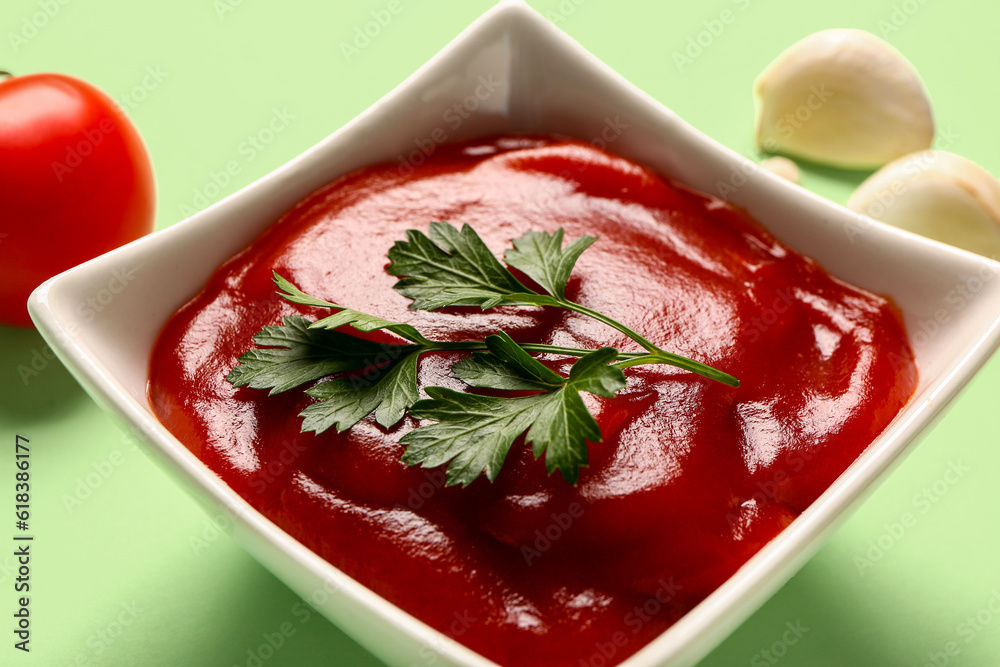 Bowl with tomato paste and fresh vegetables on green background